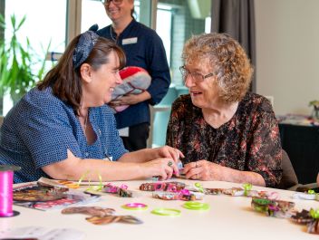 An Eldercare resident and staff member smile at each other as they make crafts together.
