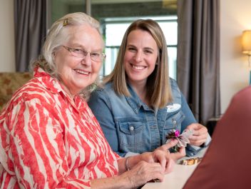Eldercare Allambi resident and volunteer smiling into the camera as they hold the crafts they are making.