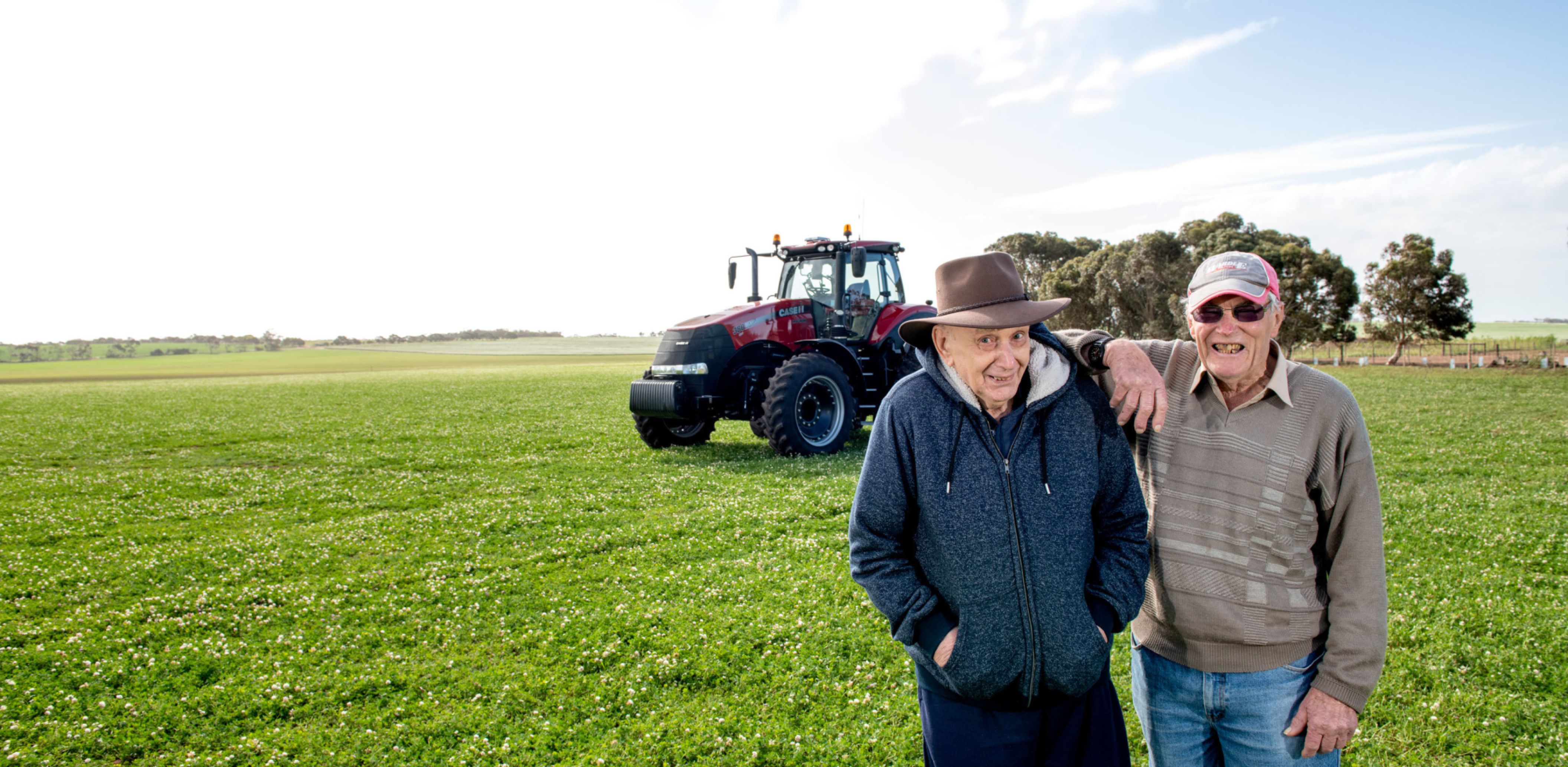 A resident and volunteer from Eldercare The Village smiling at the camera in a field in Maitland against a tractor and blue, cloudy sky.