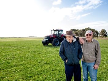 A resident and volunteer from Eldercare The Village smiling at the camera in a field in Maitland against a tractor and blue, cloudy sky.