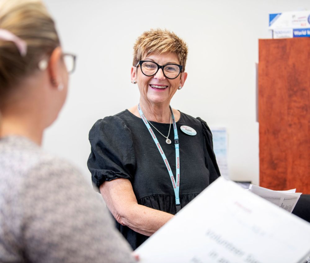 Eldercare The Lodge volunteer Pauline smiling at a colleague while filing paperwork.