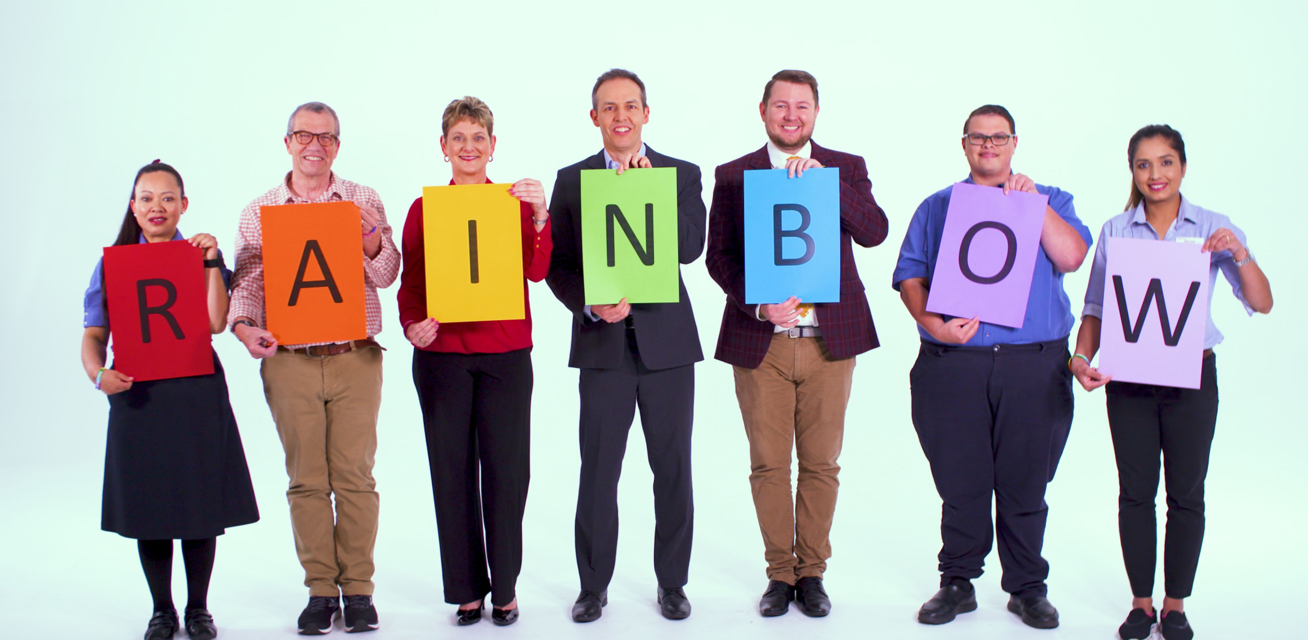 A group of Eldercare staff holding up a single letter on a coloured piece of paper with the word spelling out 'rainbow'.