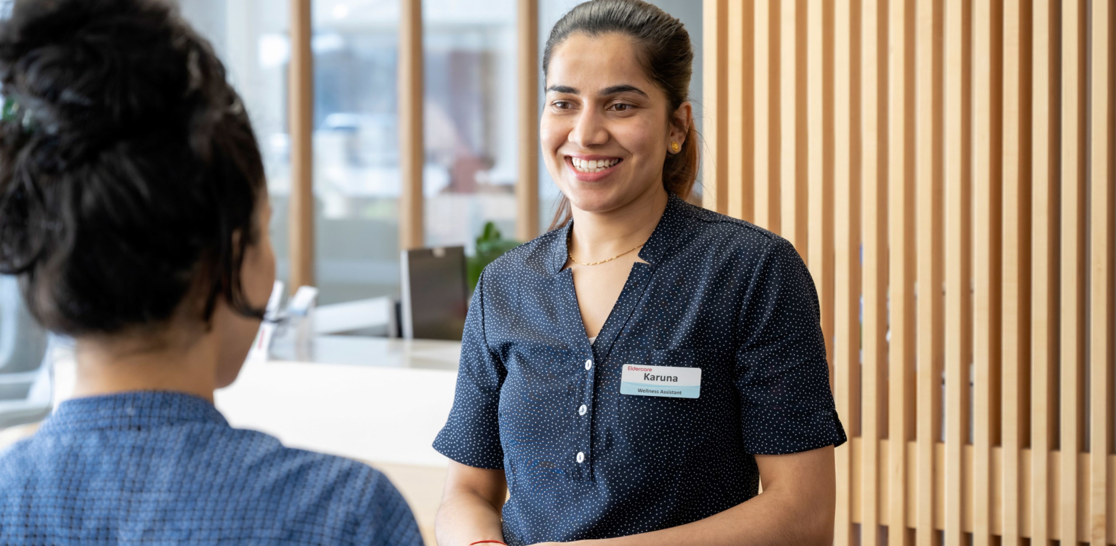 An Eldercare staff member smiles off-camera at a colleague in the reception area at an aged care home.