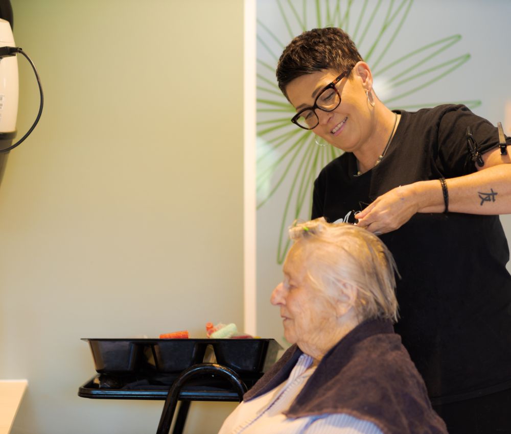 An Eldercare resident sits in the hairdressing salon while having her hair done by a professional hairdresser.