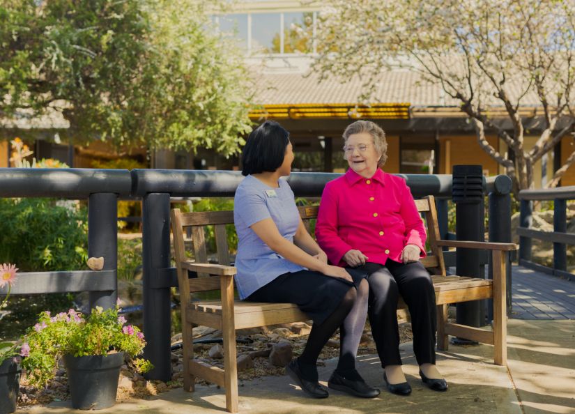 An Eldercare staff member sits with a resident on a park bench by the duck pond at Acacia Court.