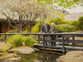 Two Eldercare residents, a couple, smile at each other while on a bridge over the duck pond at Acacia Court.