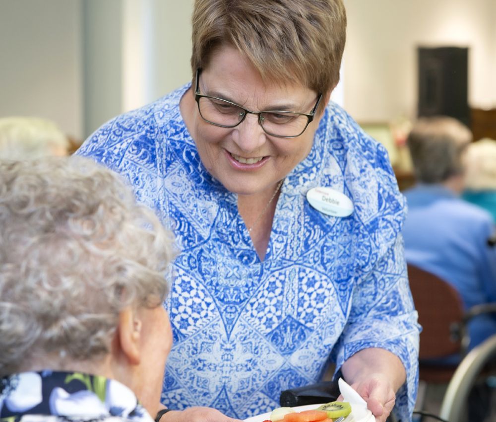 An Eldercare volunteer offers a resident a snack at happy hour.