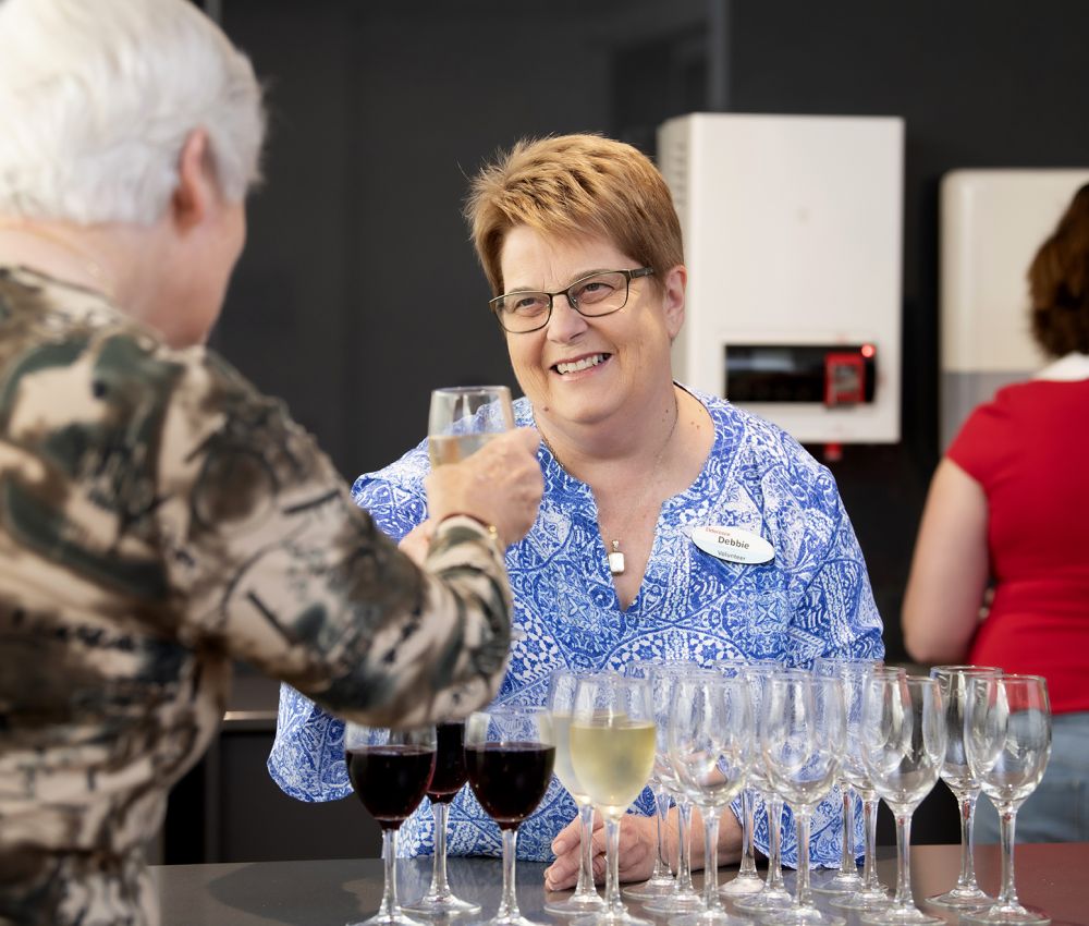 An Eldercare volunteer offers a glass of wine to an Eldercare resident at happy hour.
