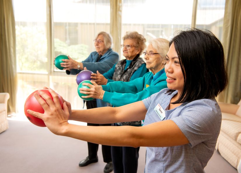 An Eldercare staff member leads three residents in a tai chi session.