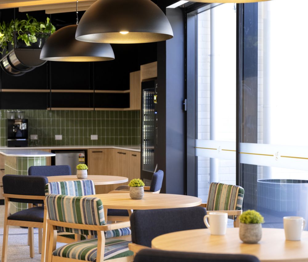 A cozy cafe area at Eldercare Goodwood aged care site, featuring tables and chairs by a large window for natural light.