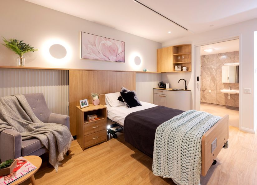 A bedroom with a neatly made bed and a plush chair.