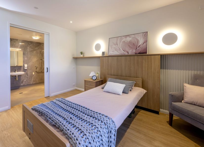 A bedroom with a neatly made bed and a plush chair.