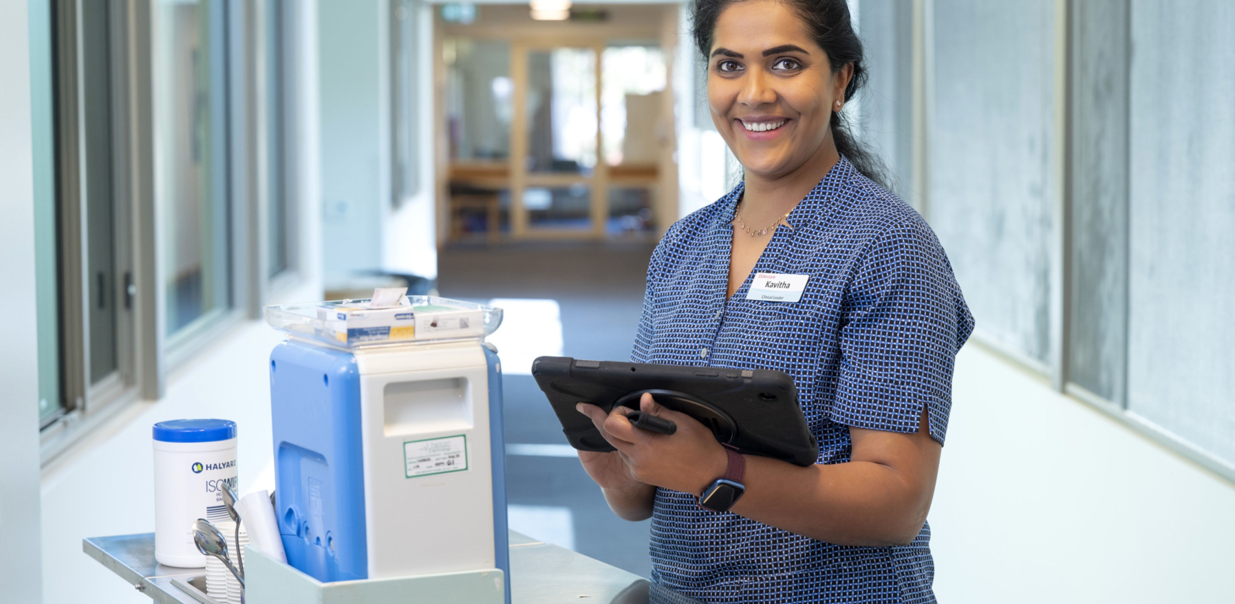 Eldercare clinical leader nurse holding a tablet while standing in a hallway.