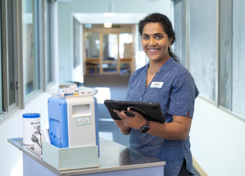 Eldercare clinical leader nurse holding a tablet while standing in a hallway.