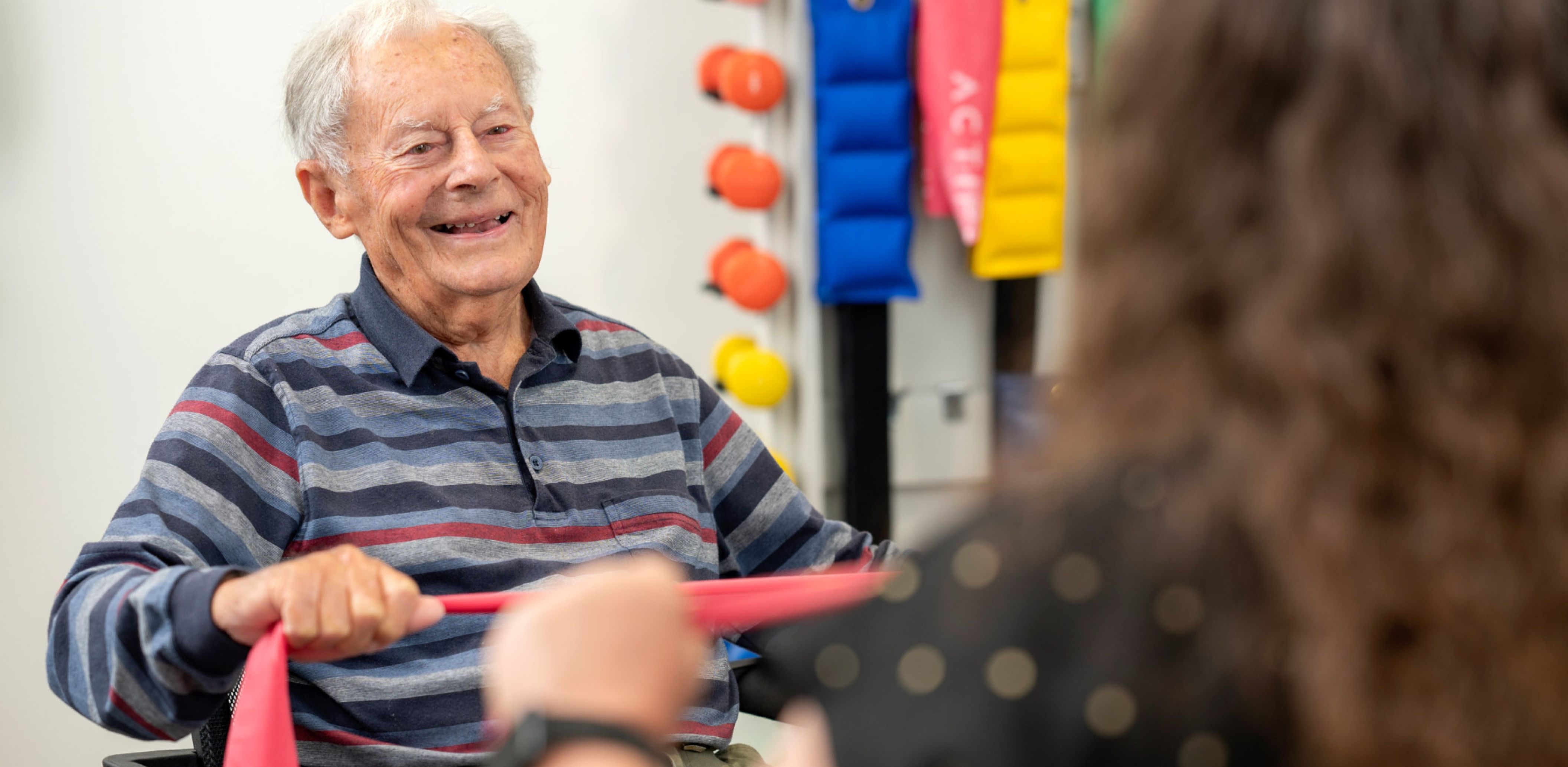A resident smiling, talks with a woman as they both engage in gym exercises.