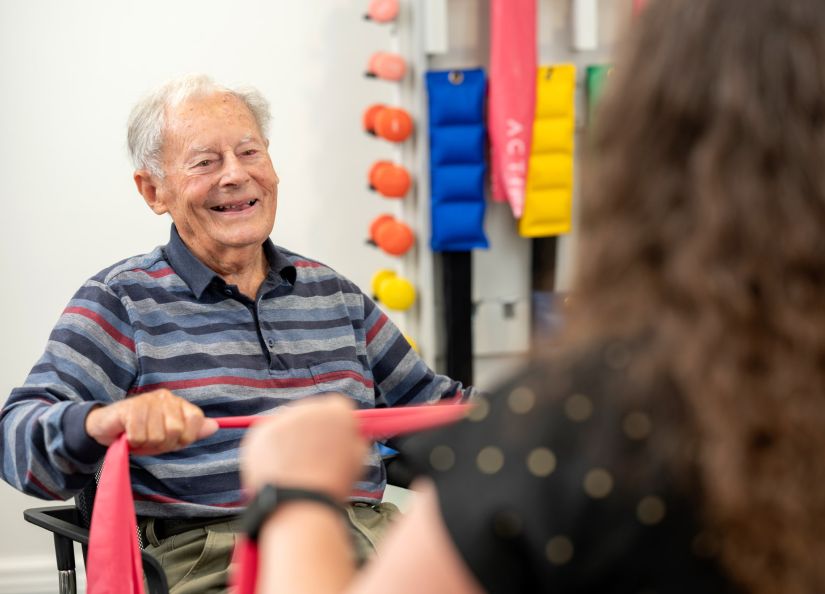 A resident smiling, talks with a woman as they both engage in gym exercises.