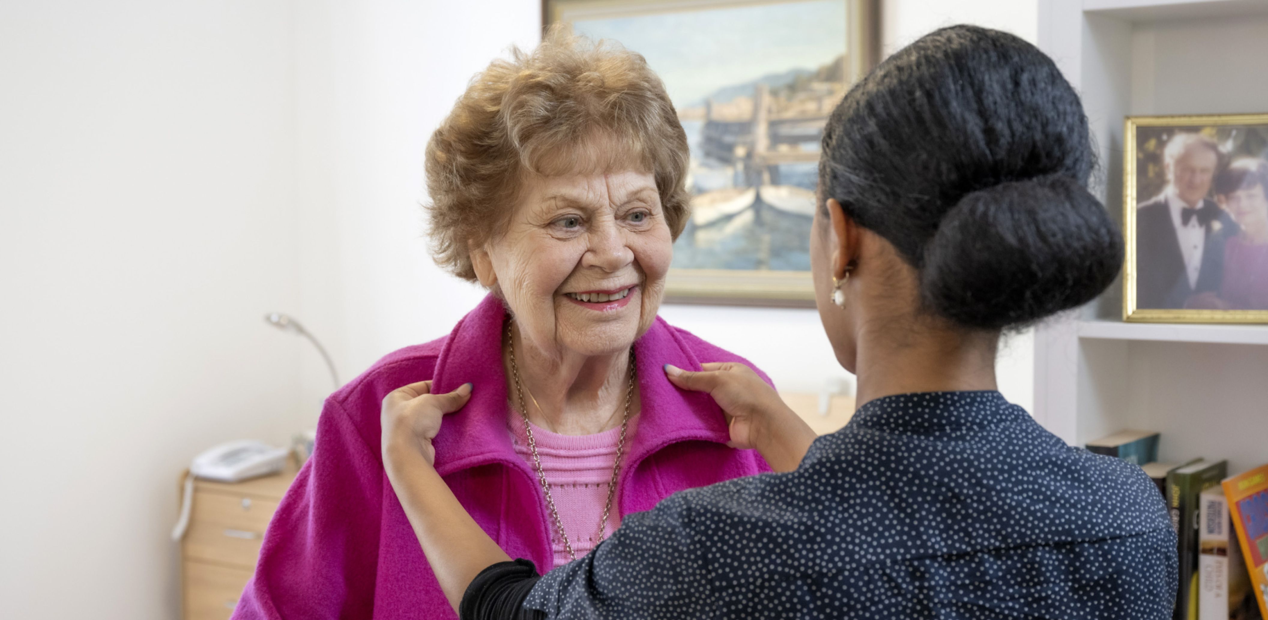 An Eldercare carer assists a resident in putting on her jacket, showcasing a moment of care.