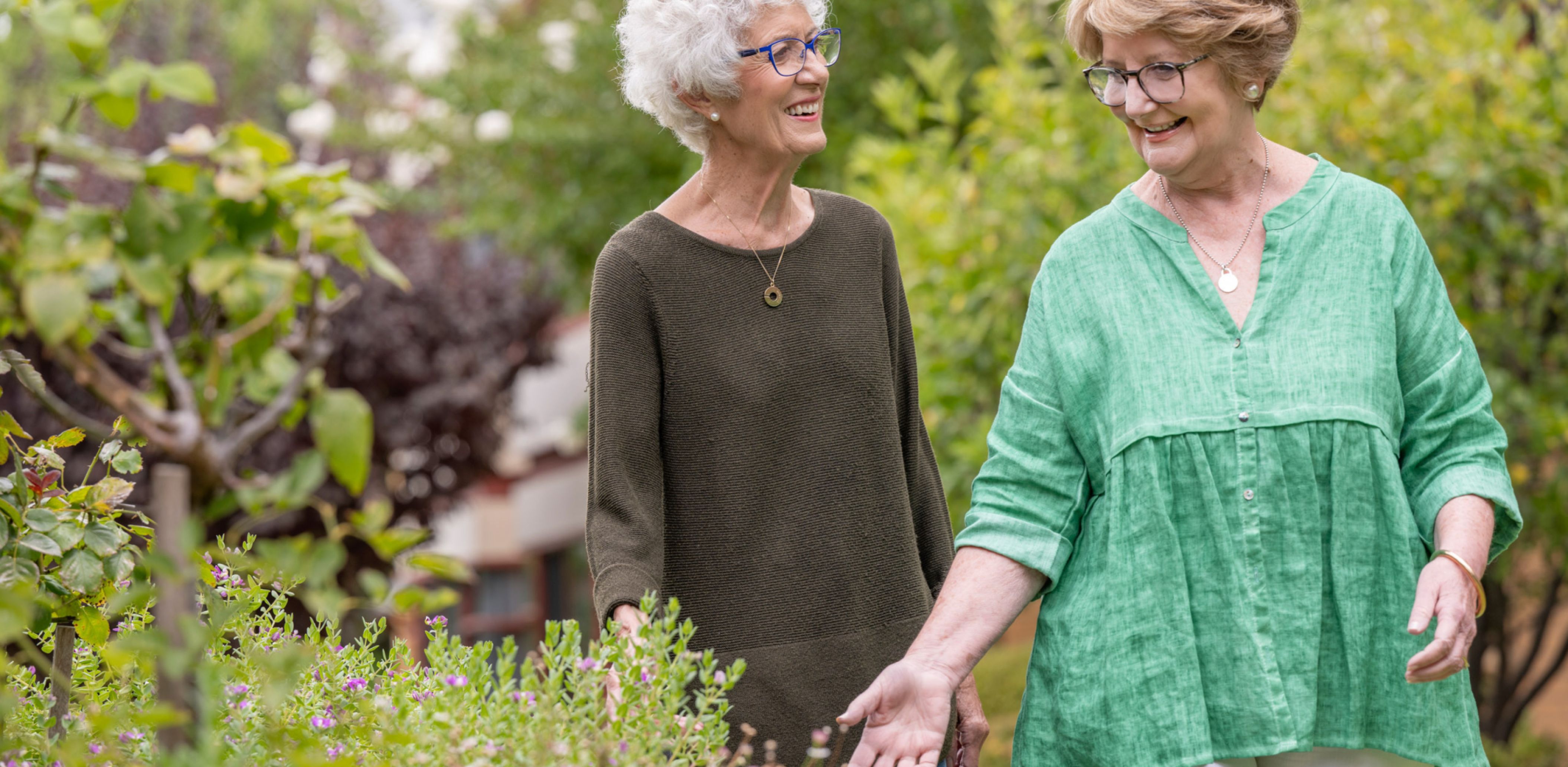 Two Eldercare residents smiling and walking in the garden.