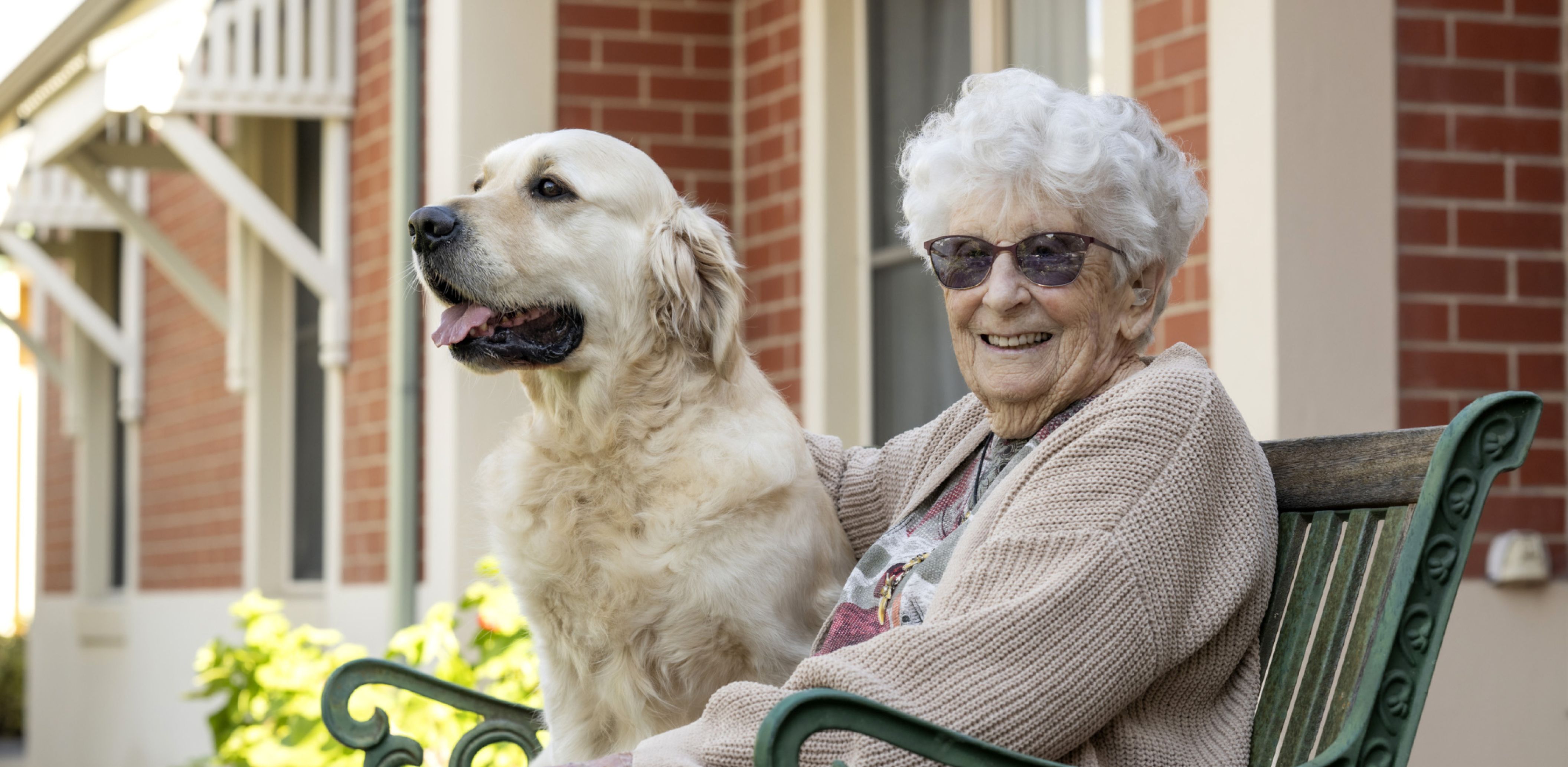 Eldercare resident sitting on a bench next to a therapy dog.