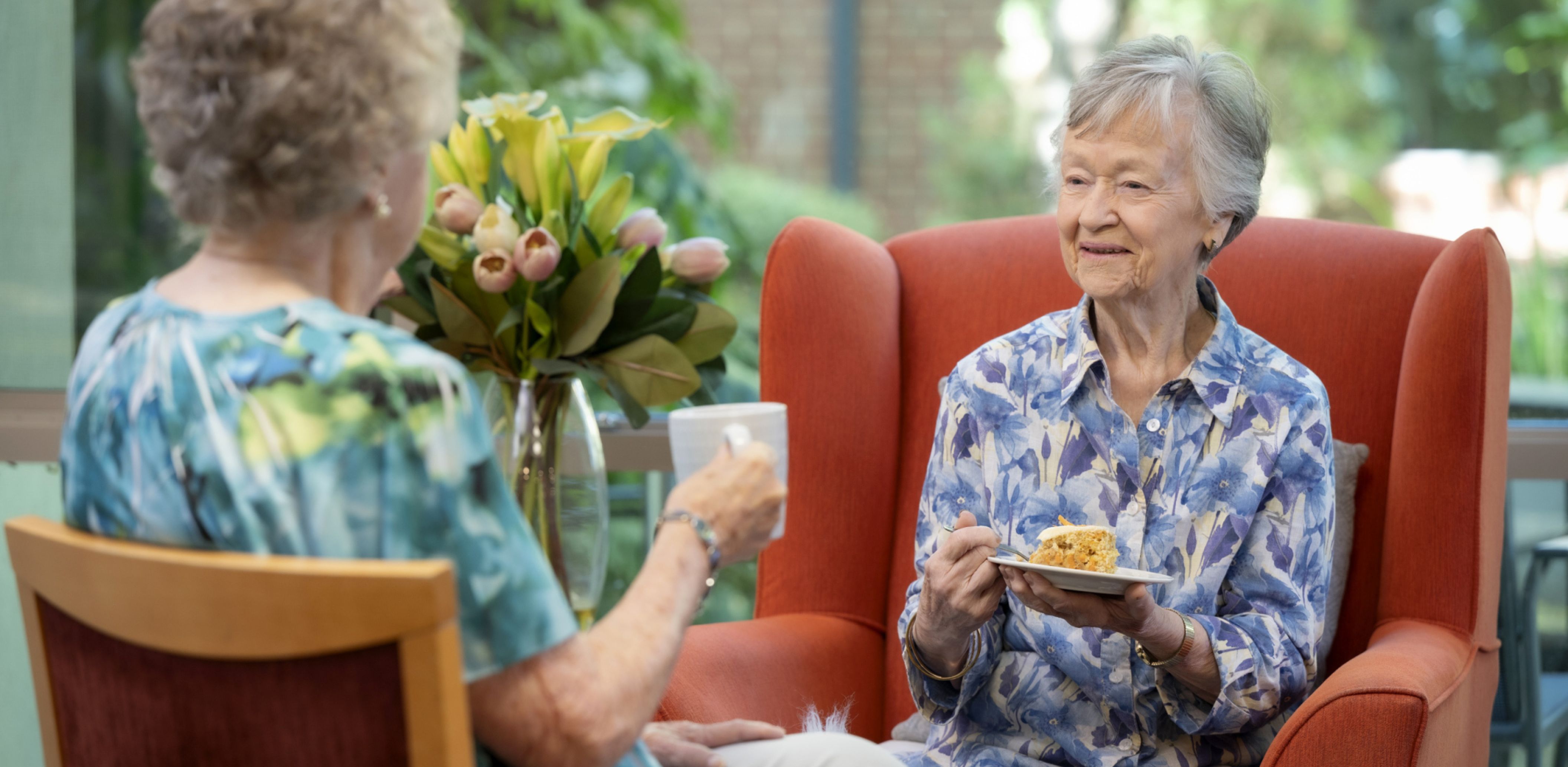 Two residents seated in chairs, enjoying a meal together and smiling.