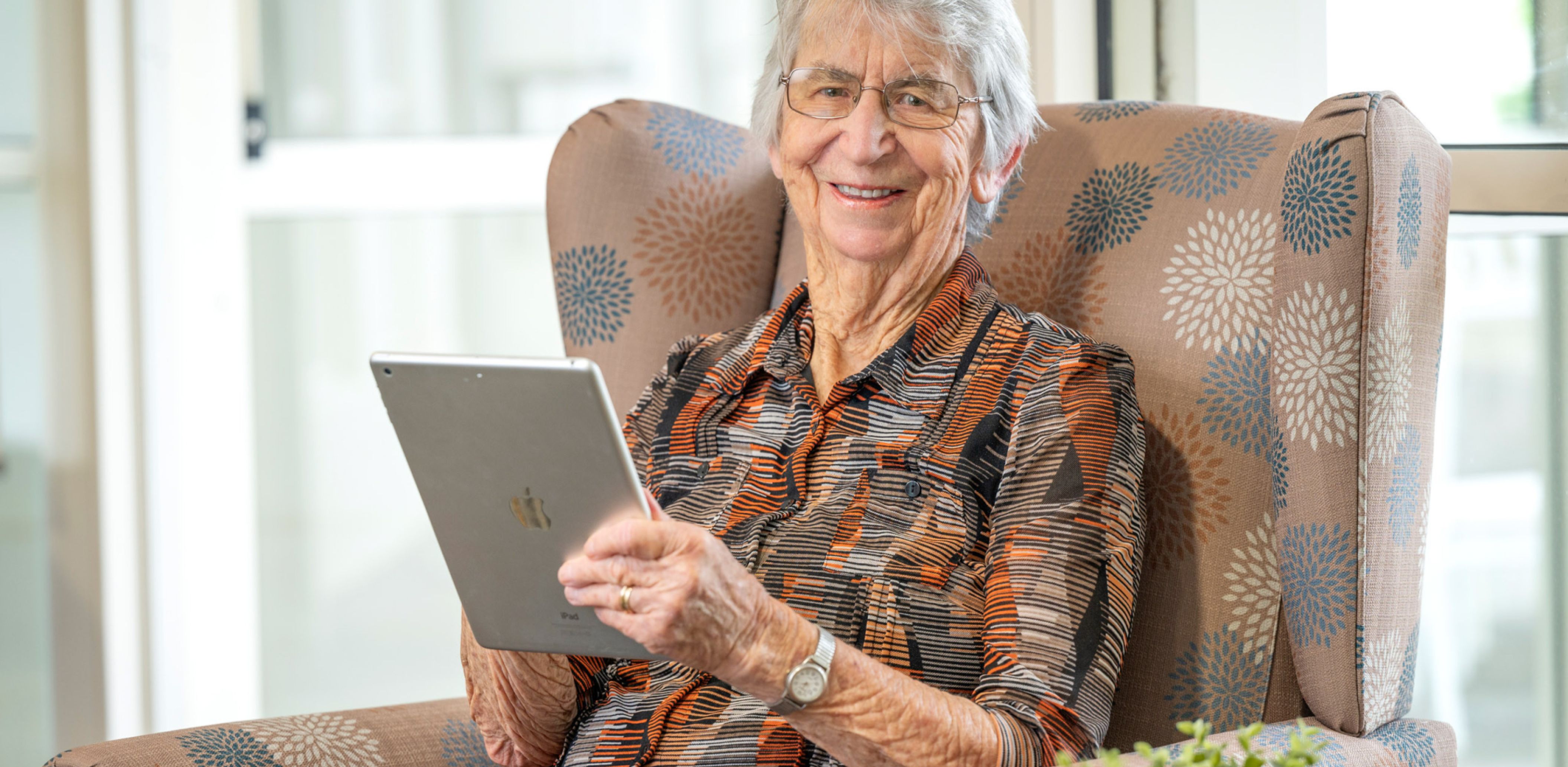 A resident sitting comfortably in a chair, focused on a tablet in her hands.