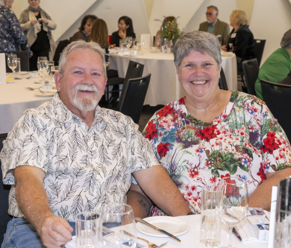 A male and a female volunteer sitting at a white round table, smiling to the camera.