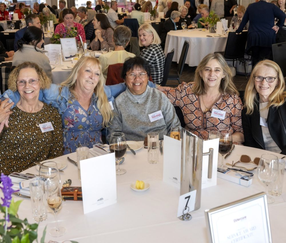 A group of volunteers sitting at a white round table, smiling at the camera.