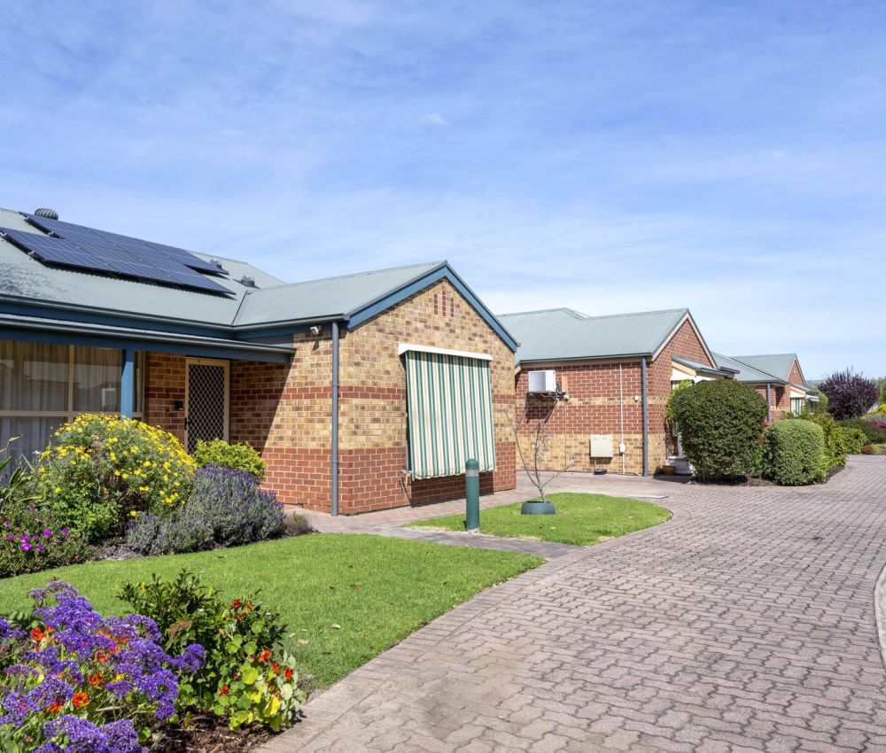 Exterior view of a retirement living community with single-storey brick homes, landscaped gardens, and a paved driveway.