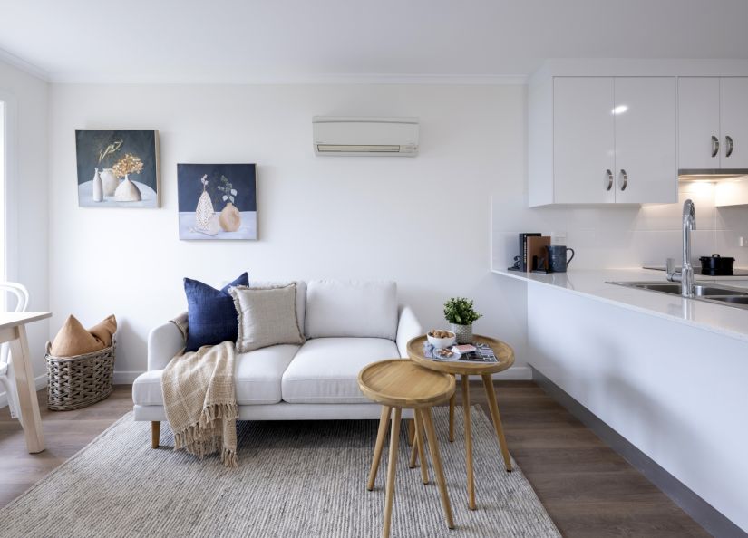 Modern living room and kitchen with a light sofa, round coffee tables, wall art, and white cabinetry with a breakfast bar.